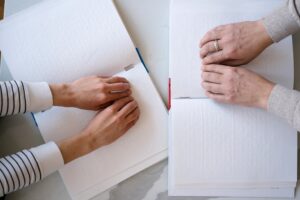 Close-up of hands reading Braille books, emphasizing touch and tactile learning.